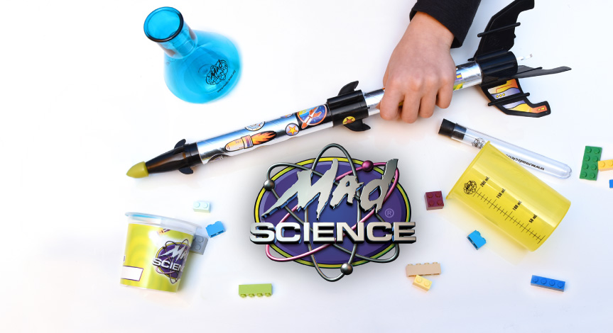 A mad science logo surrounded by Mad Science take home products such as a rocket, a flask, a beaker and a test tube