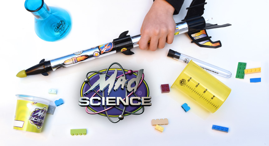 A mad science logo surrounded by Mad Science take home products such as a rocket, a flask, a beaker and a test tube