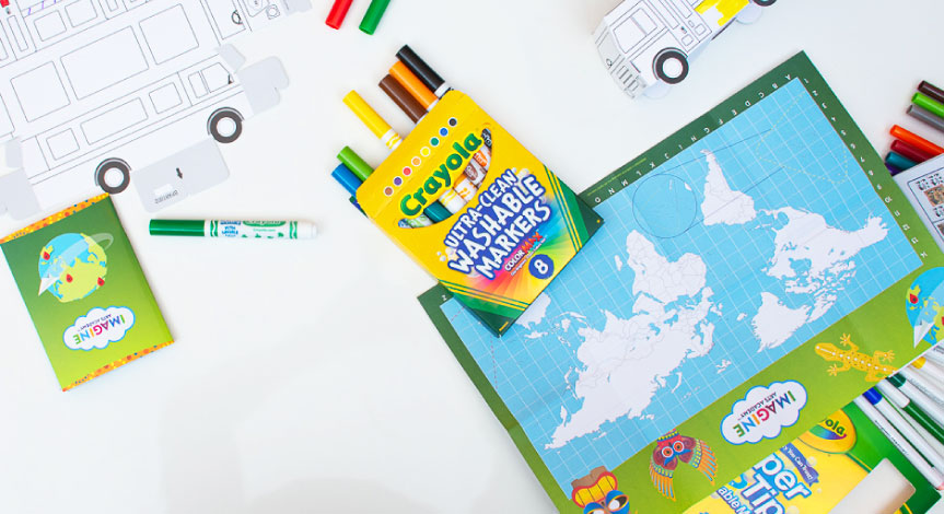 A Crayola Imagine Arts Academy map and bus take home cutout on a table with a box of Crayola washable markers.